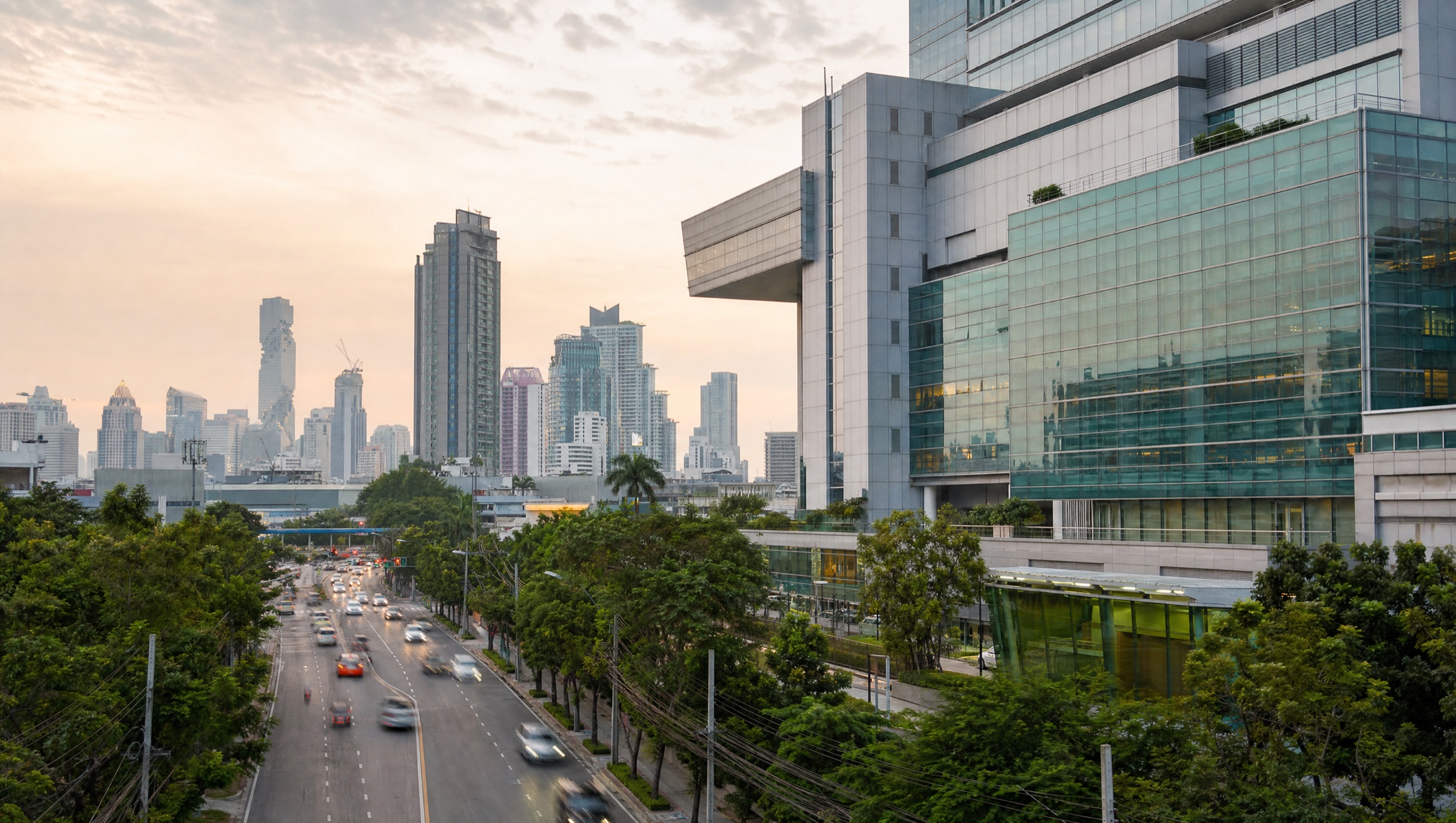 Modern hospital architecture against the Bangkok skyline at dusk.